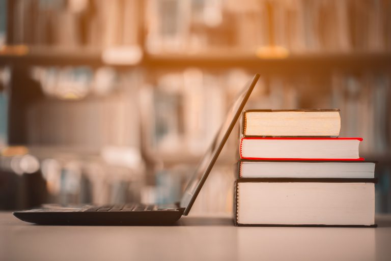 Bokhyllor och bärbara datorer placerade på ett biblioteksskrivbord. E-lärningsklass och digital e-boksteknologi.